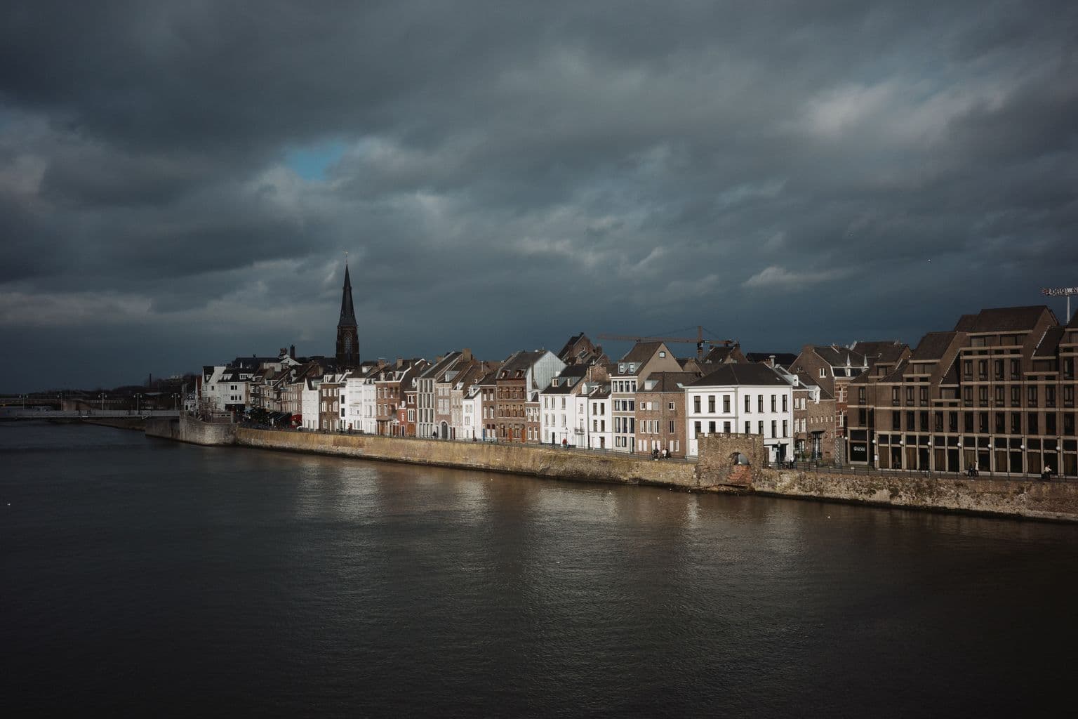 Rij bedrijfspanden aan de Maaskade van Wyck in Maastricht onder een buienlucht